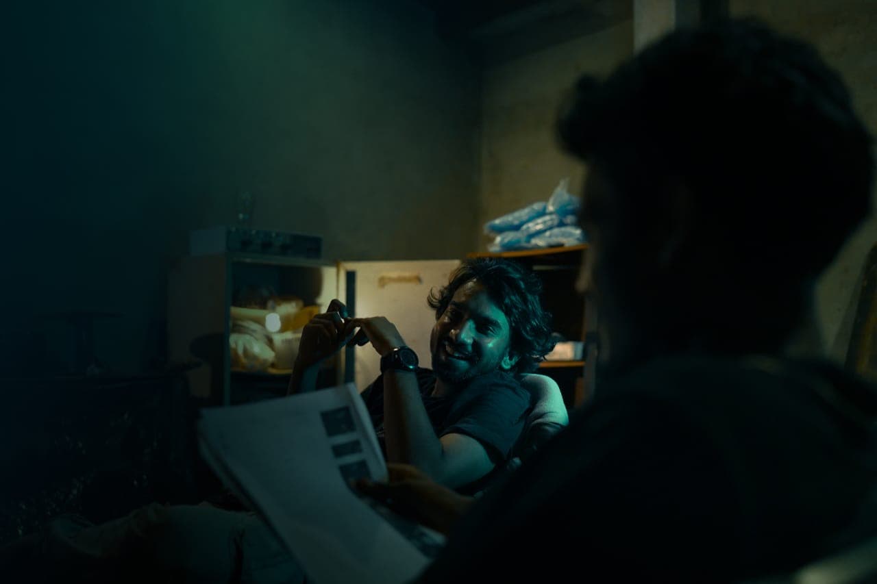 Two men in a dim room, one reading aloud from a sheaf of papers.